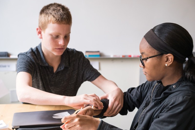 Two students learn about customizing prosthetics during class, trying on a device before assembling it.