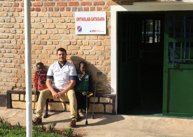 Dr. Kyle Reeser sits on a bench in Rwanda between two children with limb difference.